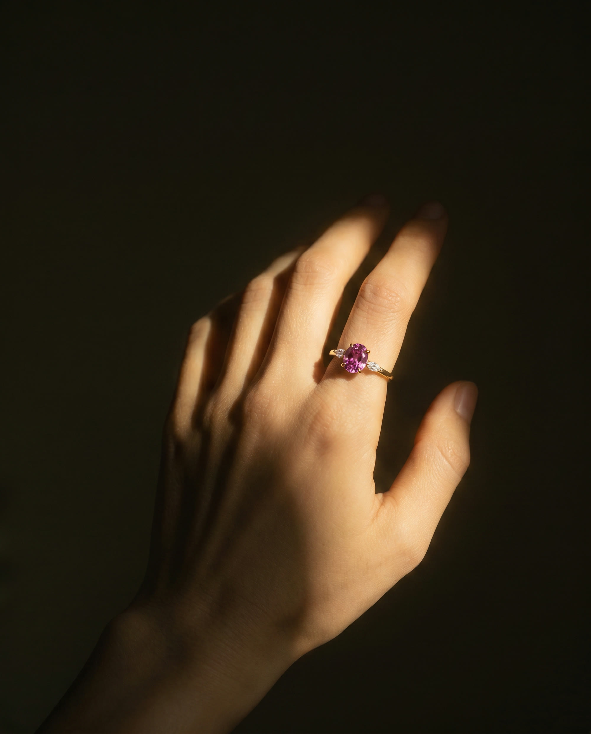A hand in deep shadow wearing a pink ring