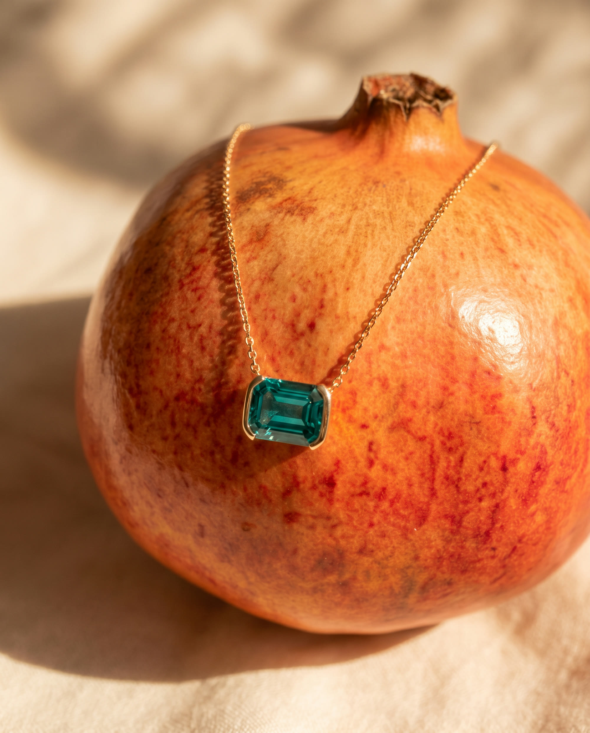 An emerald pendant draped over a sunlit pomegranate