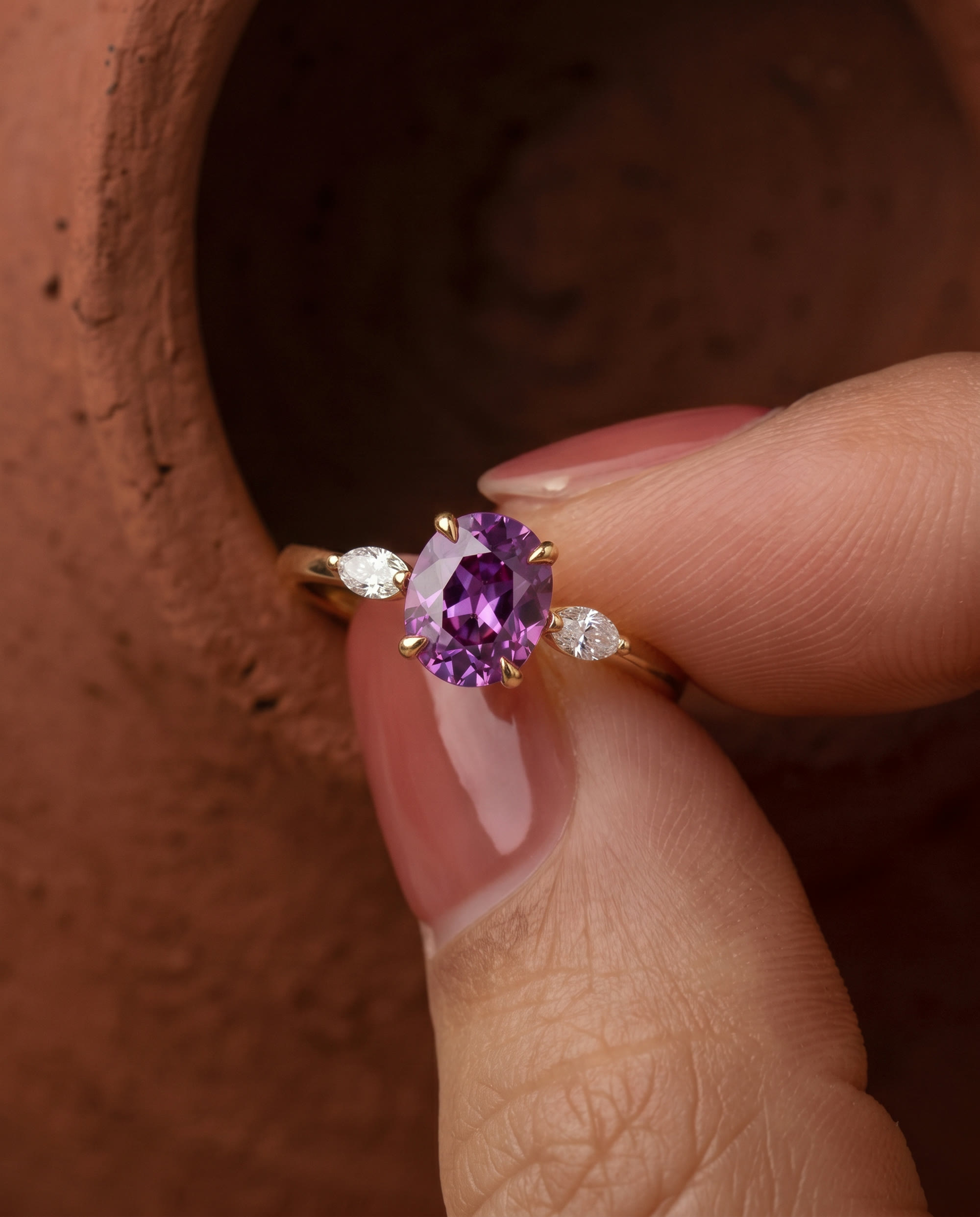 Fingertips lift an amethyst ring from a clay pot